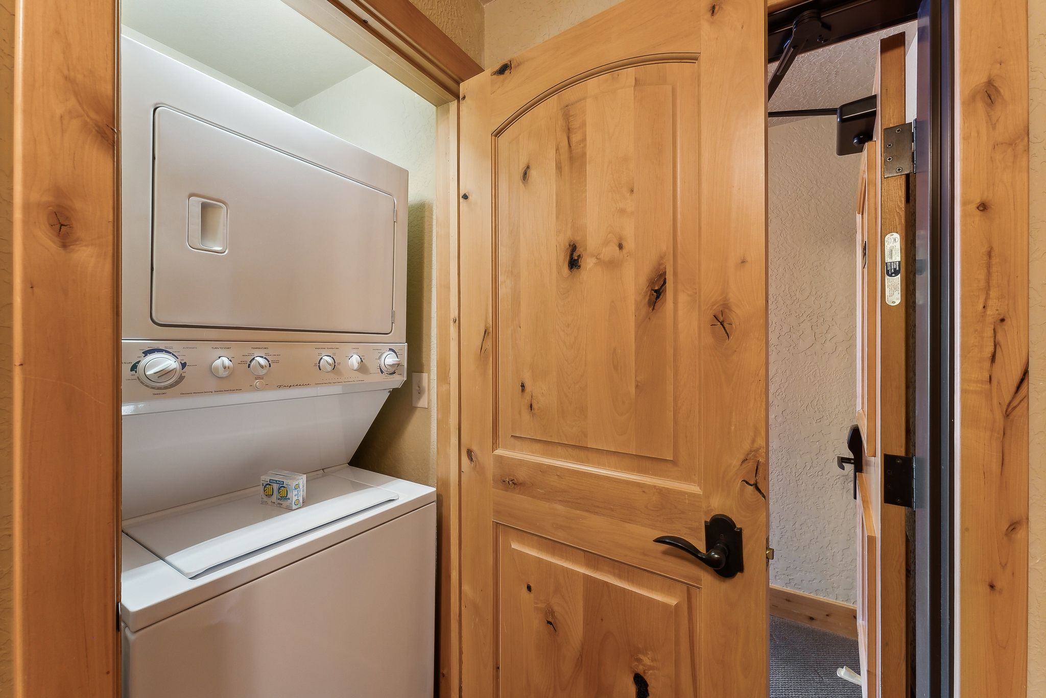 Utility closet featuring a stacked washer and dryer, wood doors with arch details, and matte black hardware
