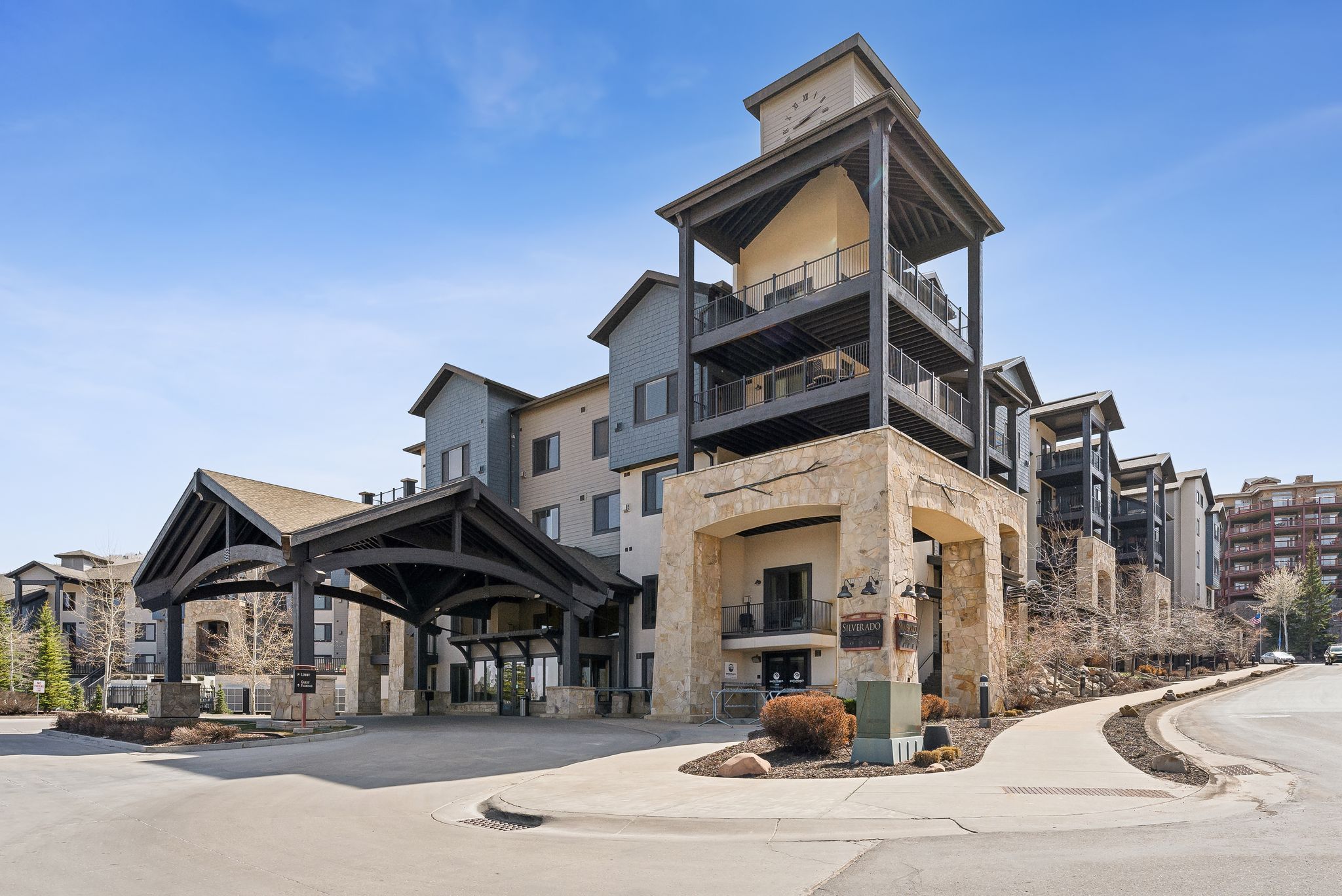 Stone and stucco exterior building featuring a porte-cochère entrance, multiple tiered balconies, and a prominent clock tower element
