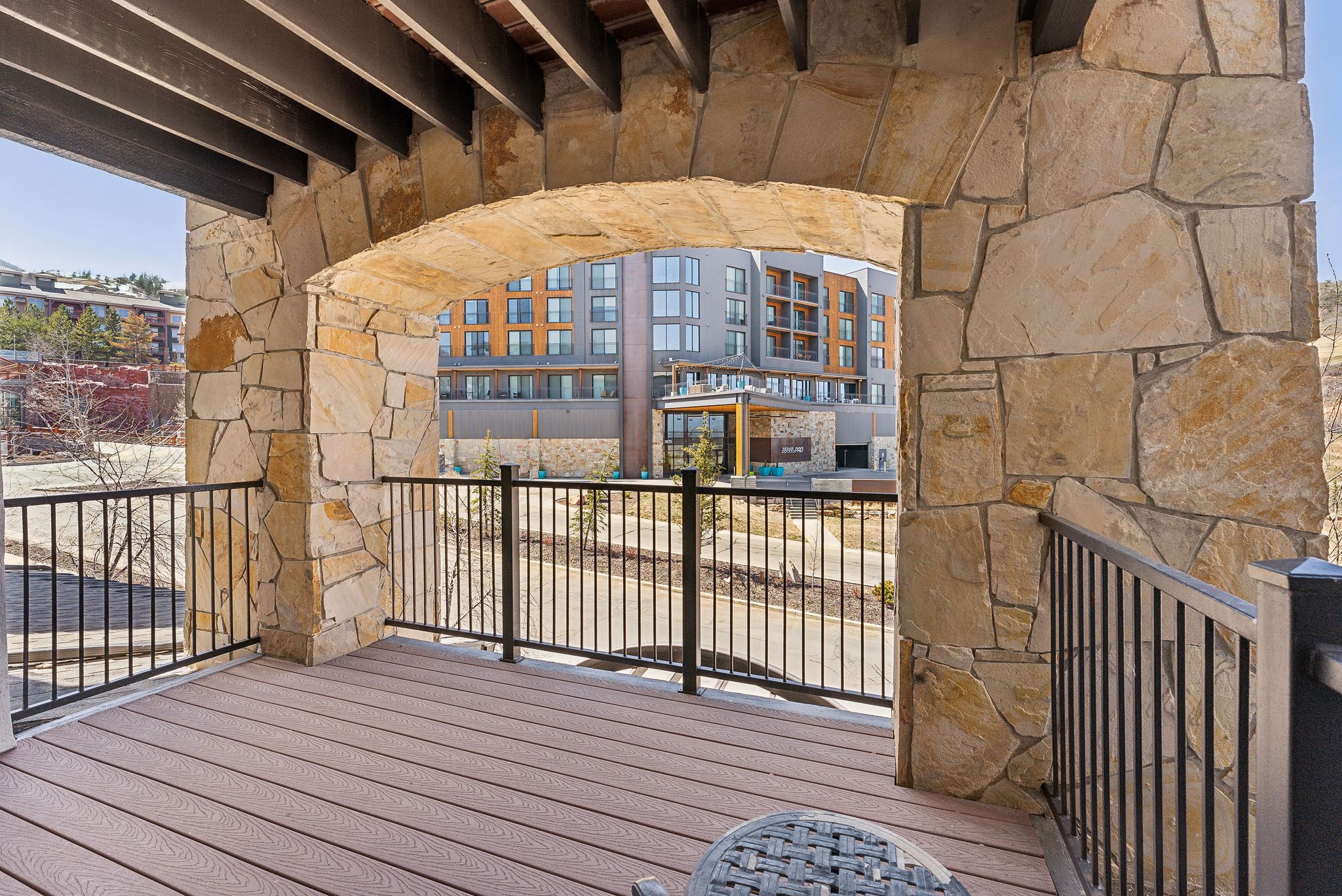 Expansive outdoor balcony featuring composite decking, black metal railings, and a stone archway