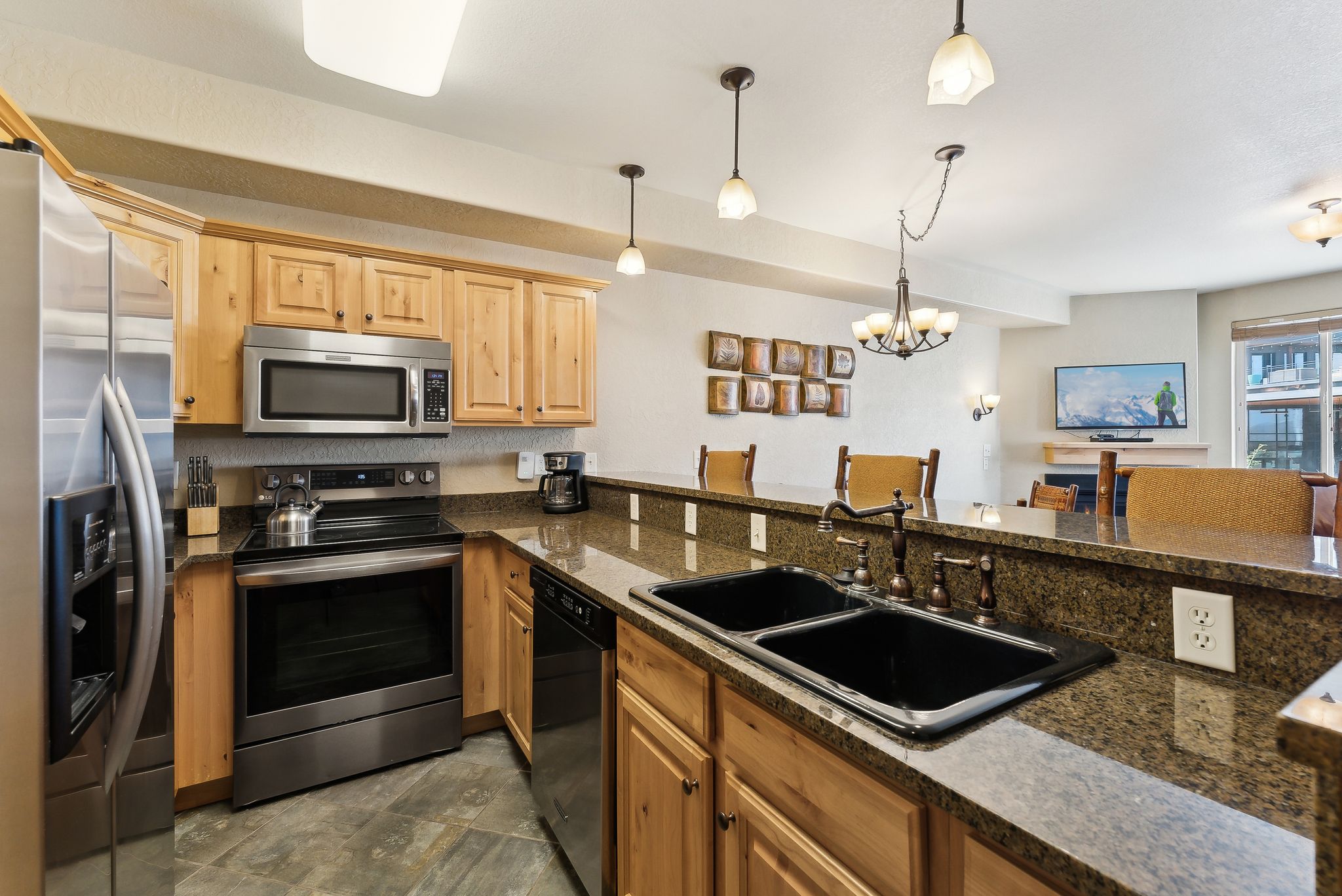 Kitchen featuring stainless steel appliances, wood cabinetry, stone countertops, and a double basin sink