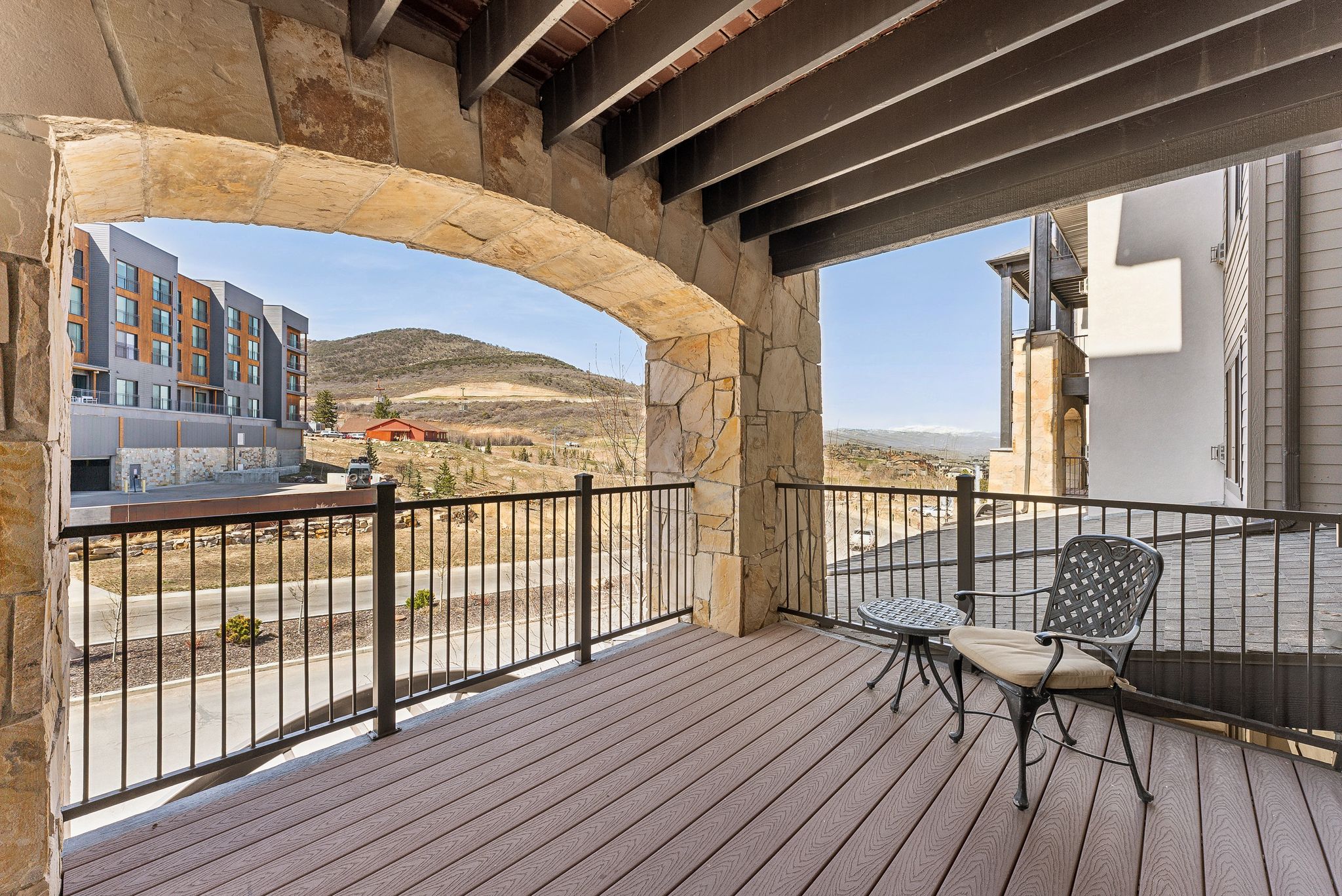Outdoor balcony featuring stone archway, wood-finish decking, and metal railings