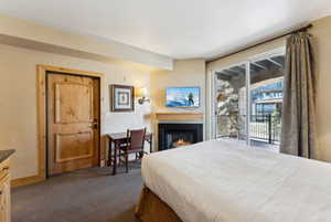Bedroom featuring dark colored carpet, access to exterior, baseboards, and a warm lit fireplace
