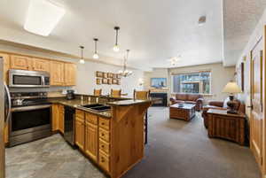Kitchen featuring a kitchen breakfast bar, a peninsula, dark countertops, stainless steel appliances, and open floor plan