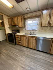 Kitchen featuring a sink, light wood-type flooring, wallpapered walls, washer / dryer, and stainless steel appliances