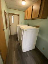 Washroom with dark wood finished floors, washing machine and clothes dryer, and cabinet space