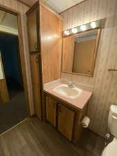 Bathroom with vanity, wallpapered walls, toilet, and wood finished floors