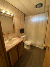 Full bath with shower / bath combination with curtain, vanity, toilet, wood finished floors, and wallpapered walls