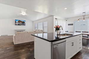 Kitchen featuring dark countertops, dark wood-type flooring, visible vents, dishwasher, and a sink