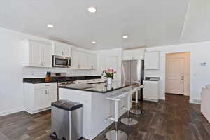 Kitchen with a sink, dark countertops, a kitchen bar, stainless steel appliances, and dark wood-type flooring