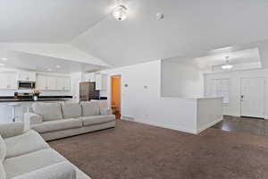 Living area featuring baseboards, vaulted ceiling, visible vents, a tray ceiling, and dark carpet