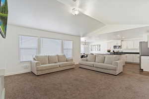 Living room with baseboards, dark colored carpet, lofted ceiling, and a wealth of natural light