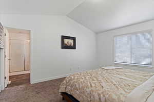 Carpeted bedroom featuring ensuite bath, baseboards, and lofted ceiling