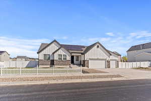 View of front facade with board and batten siding, stone siding, a fenced front yard, a garage, and roof mounted solar panels