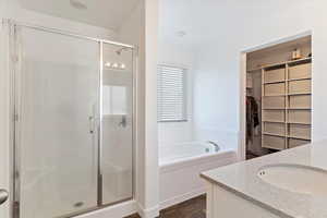 Bathroom with a bath, a spacious closet, a shower stall, vanity, and wood finished floors