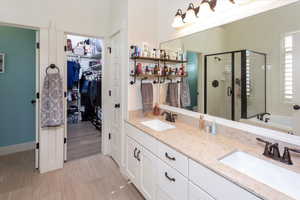 Bathroom featuring a sink, a walk in closet, a stall shower, and double vanity
