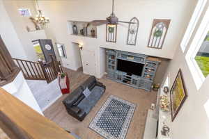 Living room featuring ceiling fan with notable chandelier, a towering ceiling, wood finished floors, stairs, and baseboards
