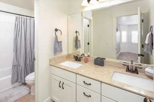 Full bathroom featuring double vanity, a sink, toilet, and shower / bath combo with shower curtain