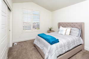 Bedroom with a closet, vaulted ceiling, visible vents, carpet floors, and baseboards