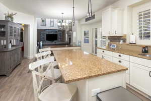Kitchen with a chandelier, light wood-type flooring, light stone counters, and white cabinets