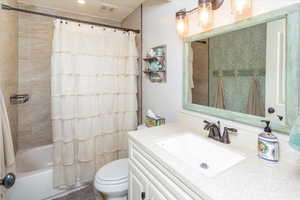 Bathroom with toilet, vanity, shower / bath combo with shower curtain, and visible vents