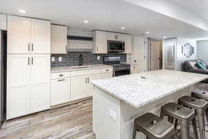 Kitchen with a kitchen breakfast bar, light wood-style flooring, a kitchen island, appliances with stainless steel finishes, and a sink
