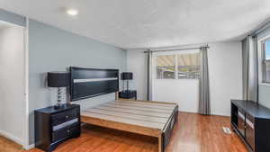 Bedroom featuring baseboards, a textured ceiling, visible vents, and light wood-type flooring