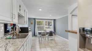 Kitchen with arched walkways, a sink, backsplash, white cabinetry, and black microwave