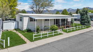 View of front facade featuring a storage unit, an outbuilding, a front lawn, a mountain view, and fence