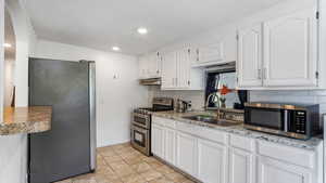 Kitchen featuring tasteful backsplash, appliances with stainless steel finishes, under cabinet range hood, and a sink