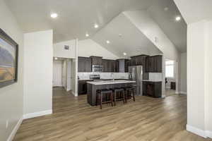 Kitchen with high vaulted ceiling, tasteful backsplash, light countertops, stainless steel appliances, and a breakfast bar area