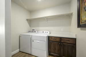 Laundry area featuring light wood-style flooring, baseboards, cabinet space, and washing machine and dryer