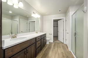 Full bathroom with double vanity, a stall shower, visible vents, a sink, and wood finished floors