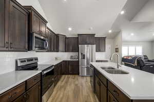 Kitchen with a sink, open floor plan, appliances with stainless steel finishes, light wood finished floors, and a center island with sink