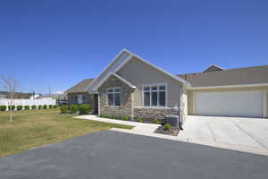 View of front of home with central air condition unit, stucco siding, stone siding, a front lawn, and driveway