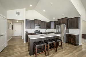 Kitchen featuring a breakfast bar, dark brown cabinets, visible vents, stainless steel appliances, and a sink