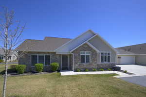 View of front of property with a front yard, central AC unit, stone siding, driveway, and roof with shingles