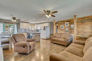 Living room with light wood-type flooring, wood walls, and ceiling fan
