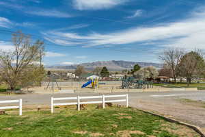 Community jungle gym featuring a mountain view, fence, and a lawn