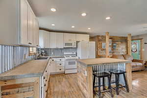 Kitchen featuring light wood-style floors, white appliances, a center island, a sink, and a breakfast bar area