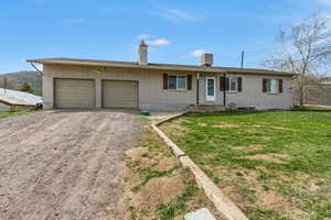 Single story home featuring a front lawn, brick siding, an attached garage, a chimney, and driveway