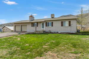 Ranch-style home featuring brick siding, a front lawn, an attached garage, and a chimney