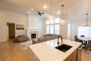 Kitchen with light stone counters, light wood-style floors, a tile fireplace, a sink, and hanging light fixtures