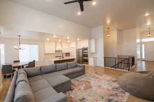Living area featuring light wood-type flooring, recessed lighting, and ceiling fan with notable chandelier
