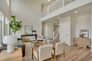PHOTOS FROM SIMILAR HOME. OPTIONS AND FINISHES WILL VARY. Living room featuring baseboards, stairway, a towering ceiling, and light wood finished floors