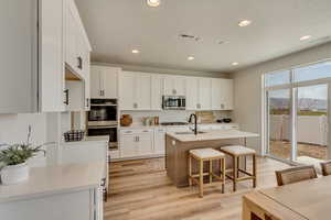 PHOTOS FROM SIMILAR HOME. OPTIONS AND FINISHES WILL VARY. Kitchen with light wood-type flooring, recessed lighting, white cabinetry, visible vents, and stainless steel appliances