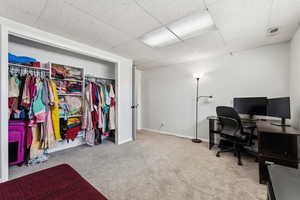 Carpeted office space with visible vents, a drop ceiling, and baseboards
