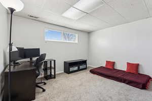 Carpeted home office with visible vents, baseboards, and a drop ceiling