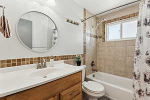Bathroom with toilet, shower / tub combo, vanity, and tile walls