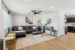 Living room featuring light wood-type flooring, baseboards, a ceiling fan, and recessed lighting