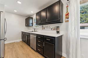 Kitchen featuring light wood-style flooring, appliances with stainless steel finishes, a sink, baseboards, and plenty of natural light